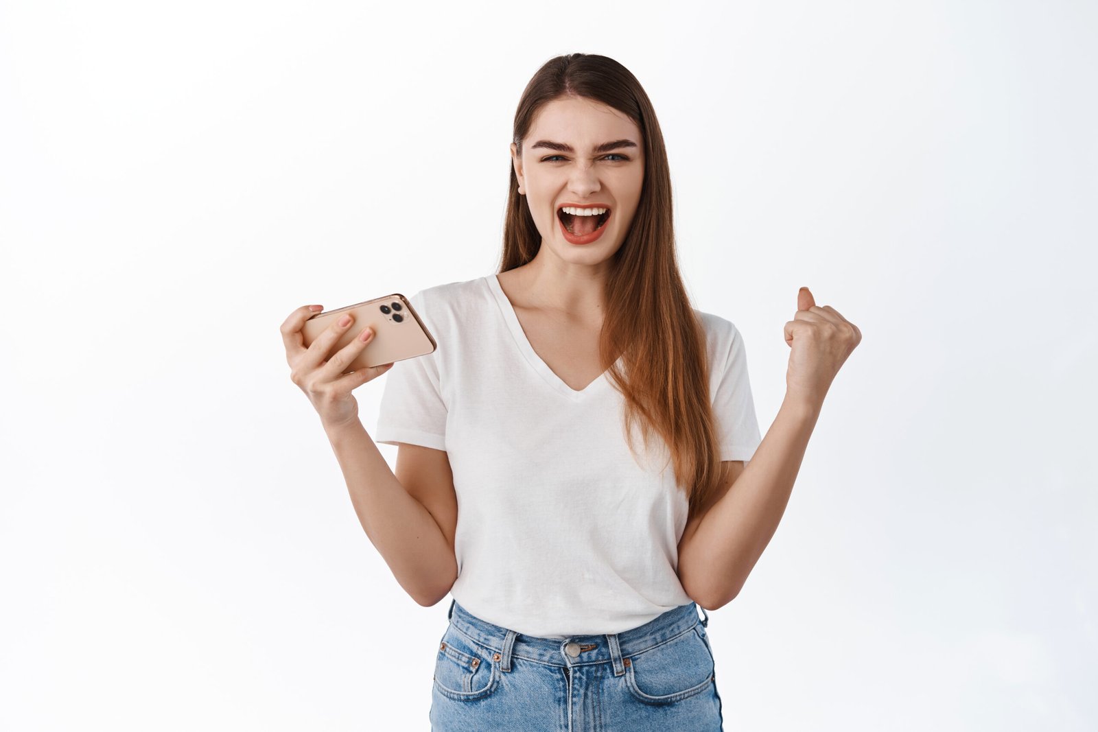 Extremely happy girl shouts yes and holds smartphone, winning on mobile game, achieve goal, networking success, celebrating victory, standing over white background.